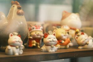 A collection of Maneki-Neko figurines with a ceramic rooster in a shop display.