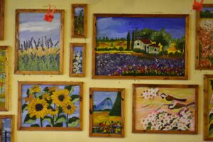 Vibrant collection of framed landscape and floral paintings on a gallery wall.