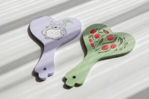 Pair of heart-shaped hand mirrors with whimsical and floral painted designs, set in warm sunlight.